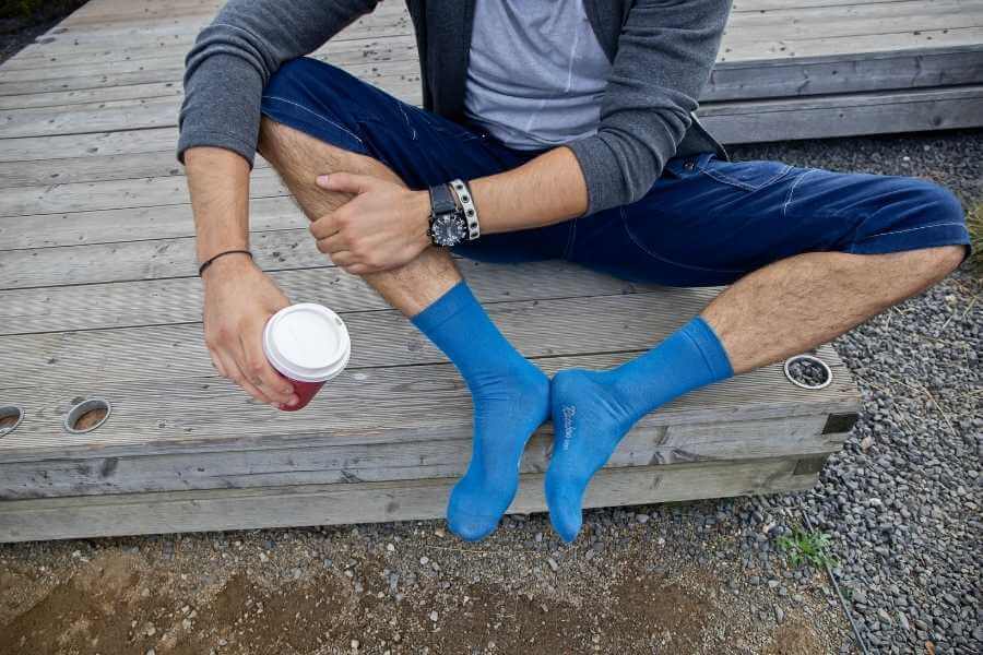 A man in blue socks sitting outdoors with a cup of coffee